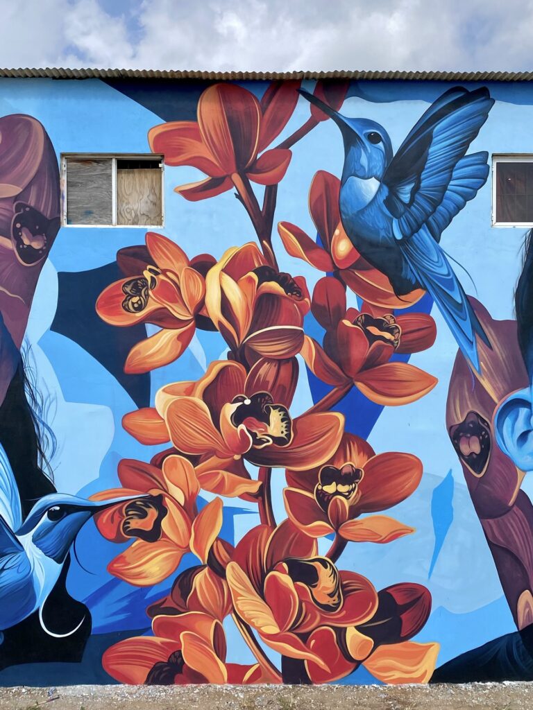 Detail of the mural Lo de aqui by Fio Silva and Sake Ink: orange flowers and two hummingbirds on blue.