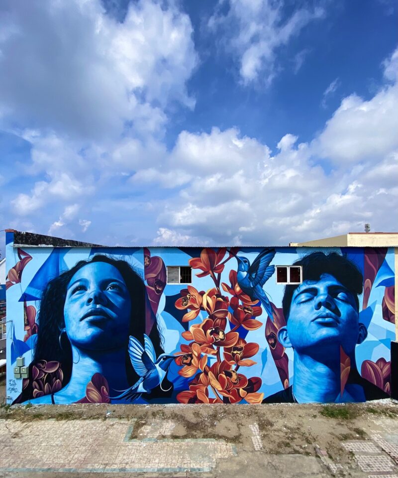 Mural Lo de aqui by Fio Silva and Sake Ink in San Nicolas, Aruba: a girl and a boy of Aruba painted in blue.