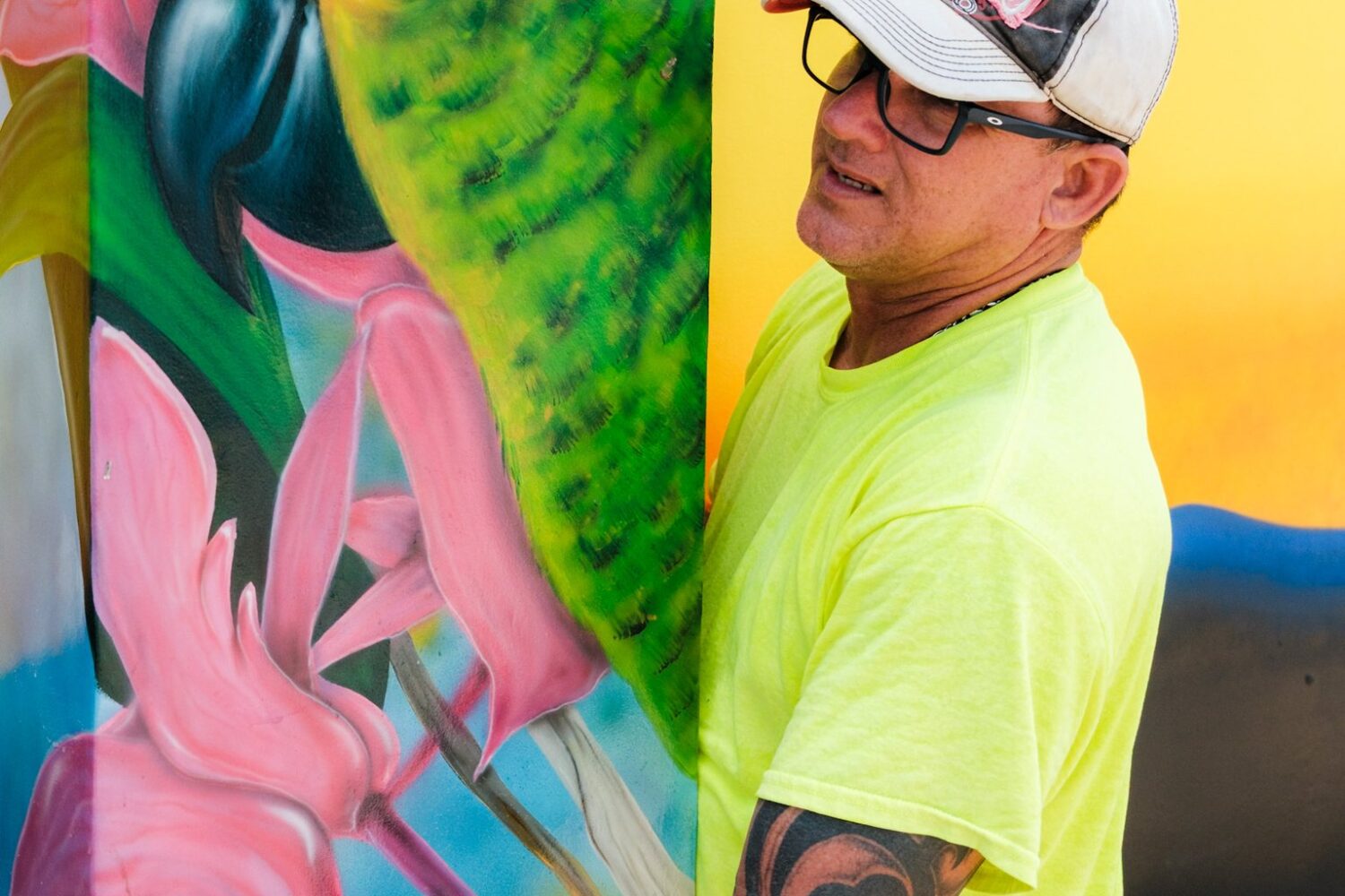 An artist standing beside a finished parrot mural during the Aruba Mural Festival 2025 in San Nicolas.